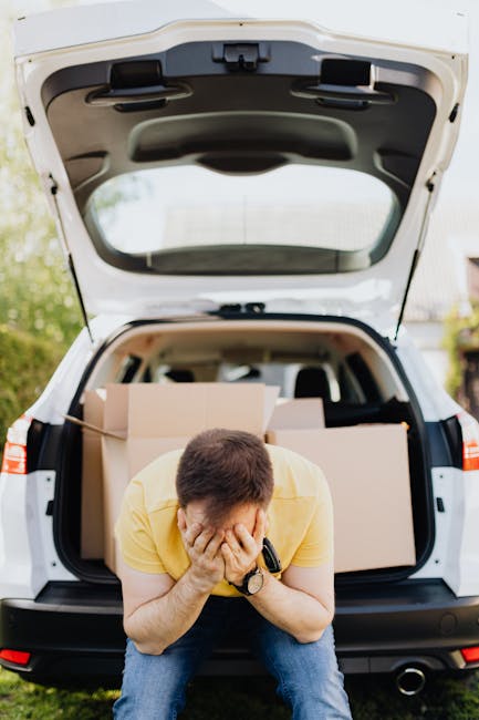A person wearing light-colored clothing is seen inside a home, arranging and stacking plain brown cardboard boxes on a wooden floor near a window with natural daylight. The individual is holding one box, preparing it for transport during a home relocation process. Several boxes are visible, some labeled with handwritten notes, indicating packed belongings such as clothes. The environment suggests an organized packing scene associated with furniture transport and moving logistics. In the background, a window provides bright natural light, illuminating the packaging area, where the individual is engaged in packing or loading boxes, potentially for a household move managed by Man with Van Maze Hill as part of their removals service. The scene captures the meticulous preparation involved in packing and moving, with the focus on the careful handling of boxes to facilitate a smooth furniture transport and home relocation.